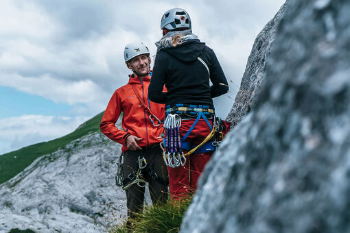 Zwei Klettercampteilnehmer stehen neben einem Berg bei bewölktem Himmel und blicken sich in die Augen.