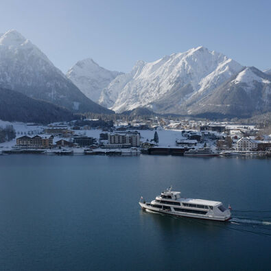 Die Achenseeschifffahrt gleitet über den See. Im Hintergrund das verschneite Pertisau am Achensee.