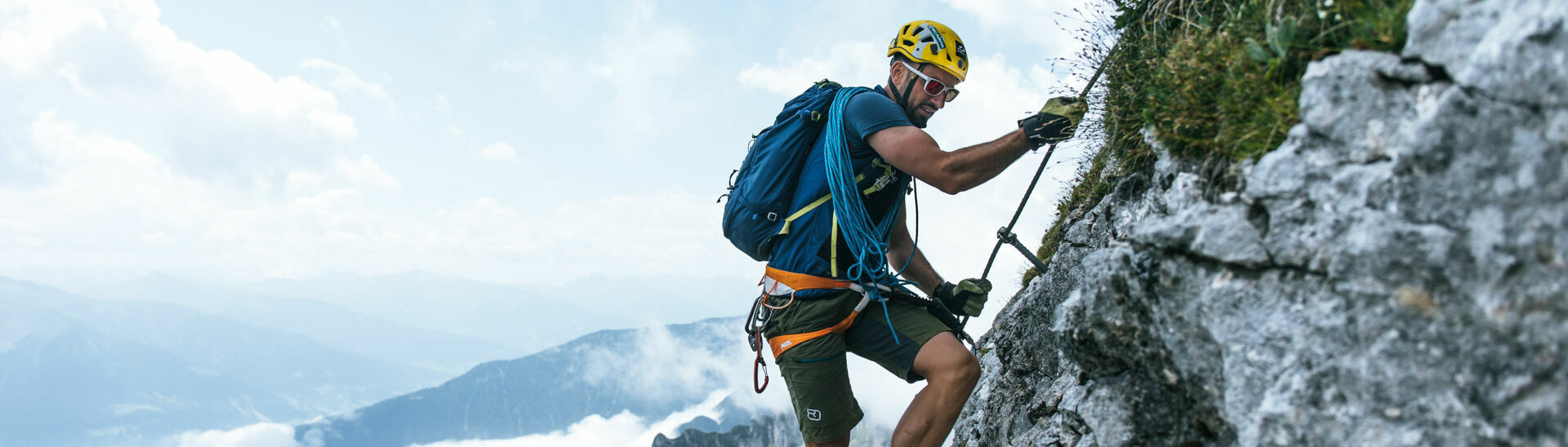 Ein Mann auf einem Klettersteig im Rofangebirge bei blauem Himmel mit vereinzelten Wolken.