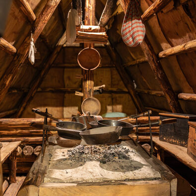 Heimatmuseum Sixenhof in Achenkirch am Achensee Eine rustikale Küche im Heimatmuseum Sixenhof. In der Mitte steht ein großer Tisch mit einem steinernen Herd, auf dem glühende Kohlen liegen. Darauf sind mehrere Pfannen platziert.