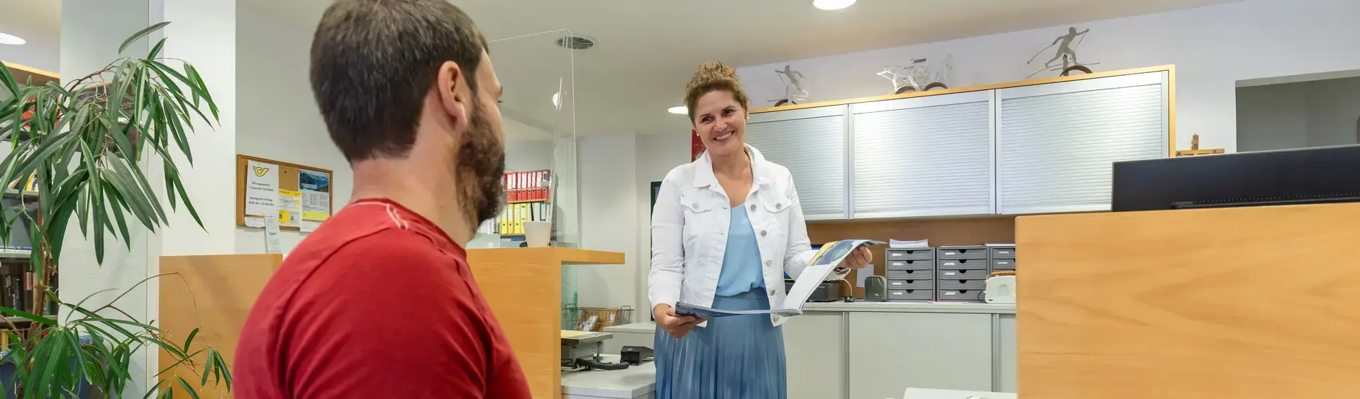 Ein Mann im Rollstuhl spricht mit einer lächelnden Frau im Barrierefreien Infobüro in Pertisau am Achensee.