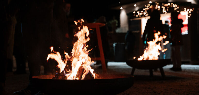 Beim Bergadvent in Pertisau brennen zwei Feuerstellen. Im Hintergrund sind Silhouetten von Menschen zu erkennen, die sich um die Feuer versammelt haben.