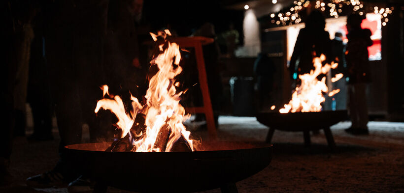 Two campfires are burning at the Mountain Advent in Pertisau. In the background, silhouettes of people gathered around the fires can be seen.