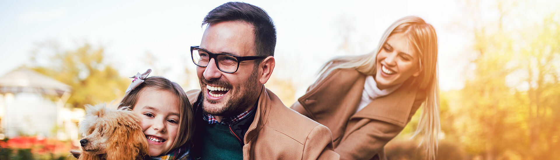 Eine lachende Familie aus einem Rollstuhlfahrer, seiner Frau, Tochter und Hund im Sommer.