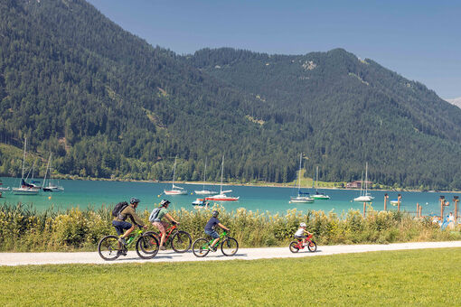 Einen Familienausflug mit dem Rad am Seeufer in Maurach am Achensee machen. Im Hintergrund sind zahlreiche Segelboote zu sehen.