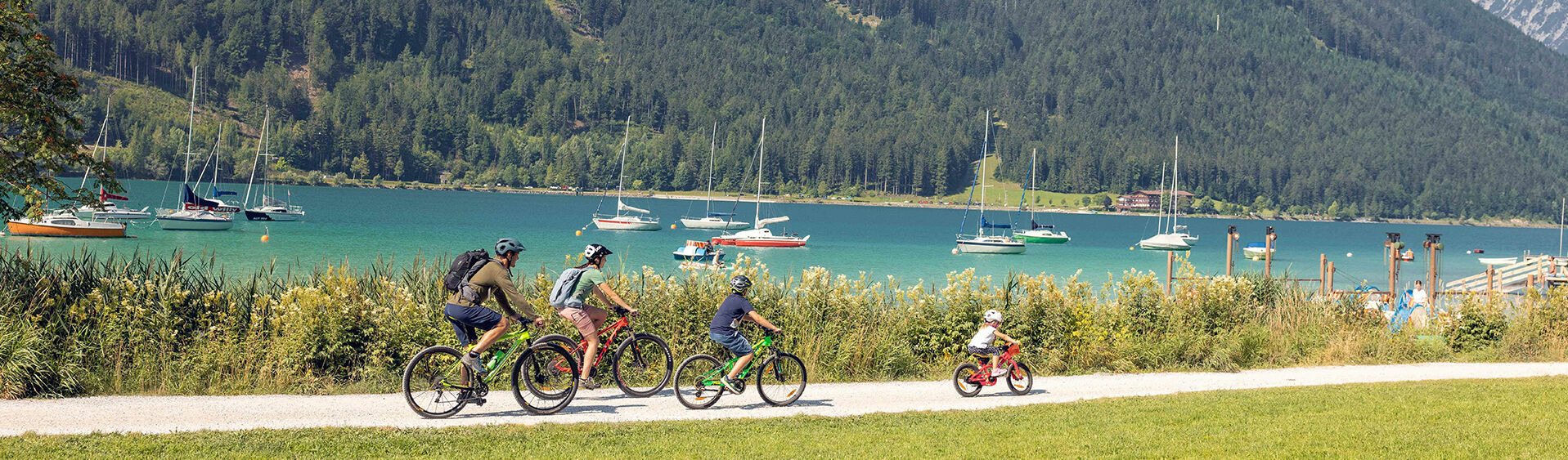 Einen Familienausflug mit dem Rad am Seeufer in Maurach am Achensee machen. Im Hintergrund sind zahlreiche Segelboote zu sehen.
