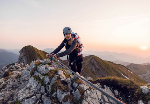 Eine bergsportbegeisterte Frau ist bei einer atemberaubenden Morgenstimmung am Klettersteig Rosskopf im Rofangebirge unterwegs.