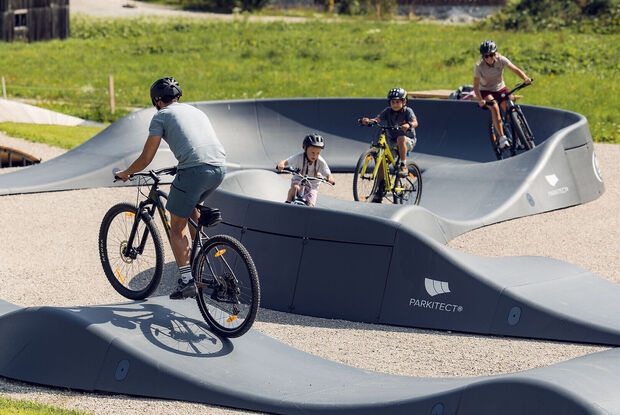 Pumptrack & Skillpark Achensee /// Pump Track & Skill Park Achensee Eine Familie ist mit ihren Fahrrädern auf dem Pumptrack in Achenkirch unterwegs. Sie nutzen den abwechslungsreichen Rundkurs zum Spielen, Bewegen und Trainieren der Fahrtechnik. /// A family is out and about on their bikes on the pump track in Achenkirch, using the varied circuit to get some exercise and practice their cycling skills.