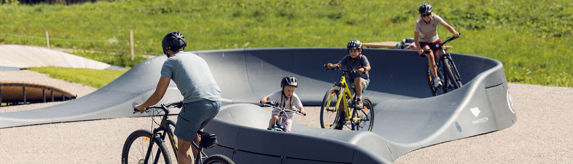 Eine Familie ist mit ihren Fahrrädern auf dem Pumptrack in Achenkirch unterwegs. Sie nutzen den abwechslungsreichen Rundkurs zum Spielen, Bewegen und Trainieren der Fahrtechnik. /// A family is out and about on their bikes on the pump track in Achenkirch, using the varied circuit to get some exercise and practice their cycling skills.