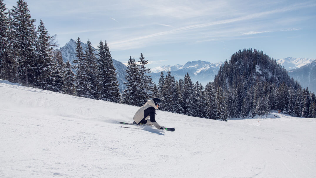 A skier enjoys the sunny winter day on the perfectly groomed slopes of the Rofan mountains overlooking the Nature Park Karwendel.