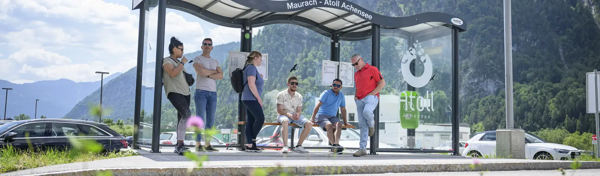 Eine Gruppe Männer und Frauen warten auf den nächsten Bus bei der Haltestelle des Atoll Achensee.