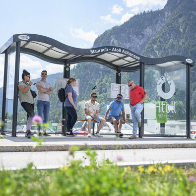 Eine Gruppe Männer und Frauen warten auf den nächsten Bus bei der Haltestelle des Atoll Achensee.