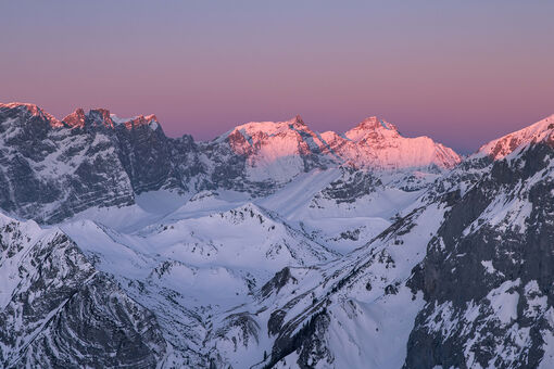 Der Blick auf den winterlichen Naturpark Karwendel bei Sonnenaufgang ist magisch. Die Gipfel und der Himmel färben sich violett und rosarot.