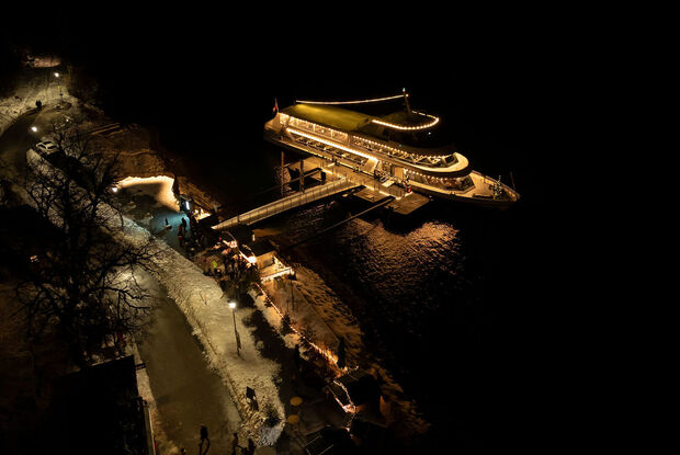 Die Landweihnacht und die Achenseeschifffahrt erstrahlen bei Nacht an der Schiffsanlegestelle Scholastika in Achenkirch. /// This photo captures the onshore Christmas market and the Scholastika pier in Achenkirch illuminated at night.