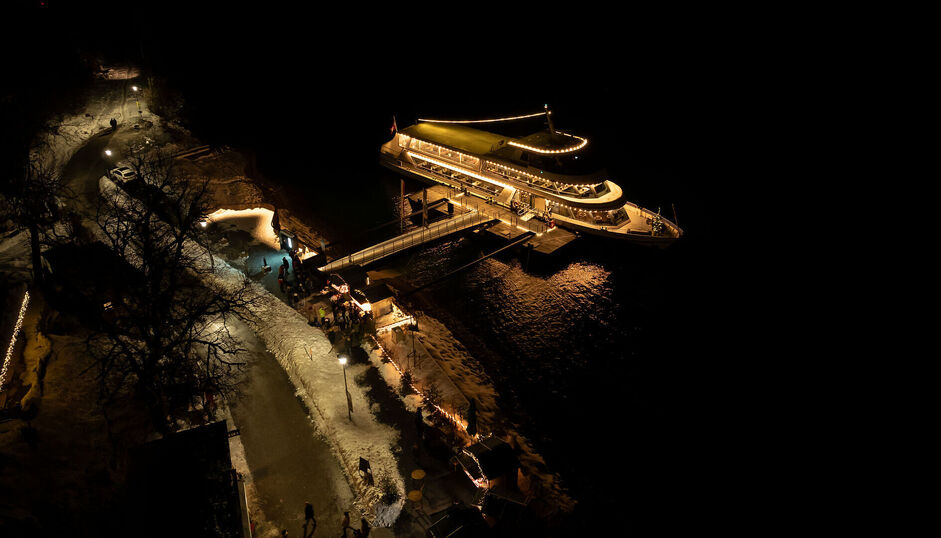 Die Landweihnacht und die Achenseeschifffahrt erstrahlen bei Nacht an der Schiffsanlegestelle Scholastika in Achenkirch. /// This photo captures the onshore Christmas market and the Scholastika pier in Achenkirch illuminated at night.