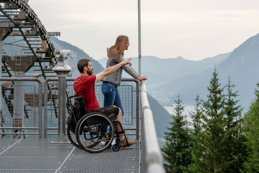 Ein Mann im Rollstuhl und seine Freundin genießen den Ausblick vom Zwölferkopf auf die Region Achensee im Sommer..