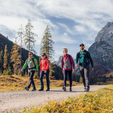 Eine Gruppe von Freunden nutzt das schöne Wetter für eine Herbstwanderung durch das bunt gefärbte Falzthurntal im Naturpark Karwendel.