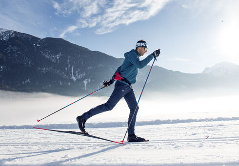 In sunny weather, a cross-country skier is skiing classic style on the village trail in Achenkirch.