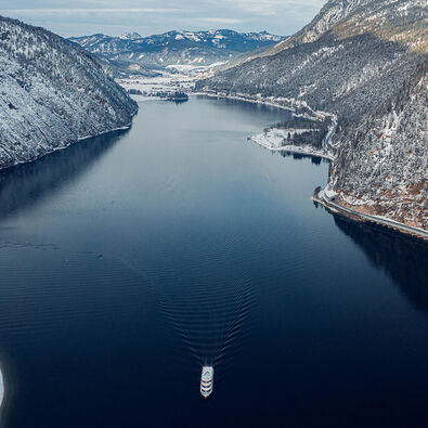 Blick auf den winterlichen Achensee und das Dorf Achenkirch. Auf dem Achensee fährt ein Schiff der Achenseeschifffahrt.