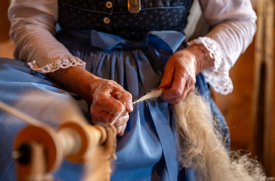 Beim Achentaler Kirchtag im Heimatmuseum Achental - Sixenhof zeigen Bäuerinnen handwerkliche Techniken wie hier am Spinnrad.
