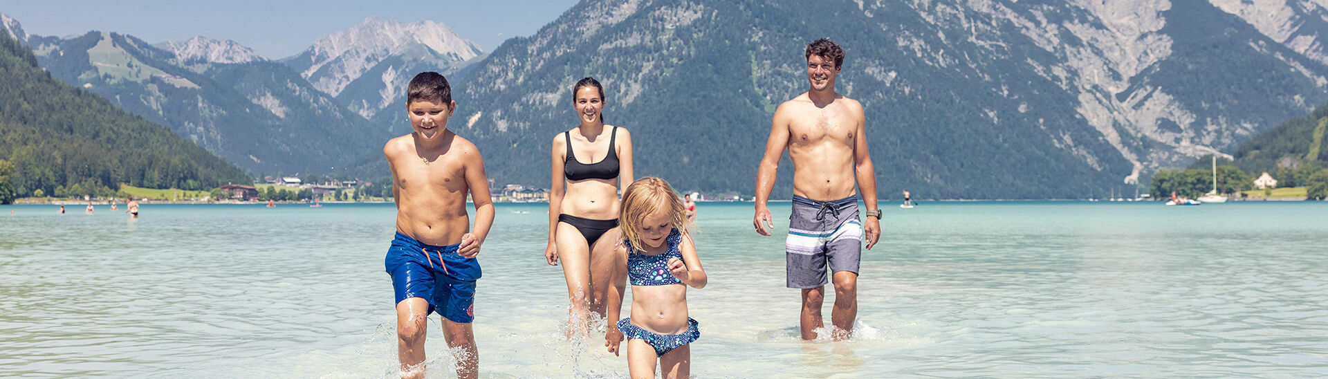 A family with children bathing in the turquoise blue Lake Achensee in Maurach and enjoying the sunny weather.