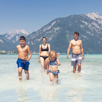 Eine Familie genießt das schöne Wetter und badet im türkisblauen Achensee in Maurach.