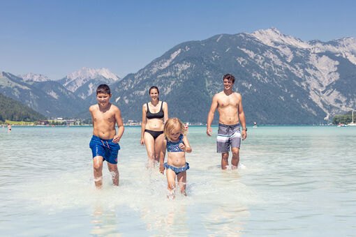 Eine Familie genießt das schöne Wetter und badet im türkisblauen Achensee in Maurach.