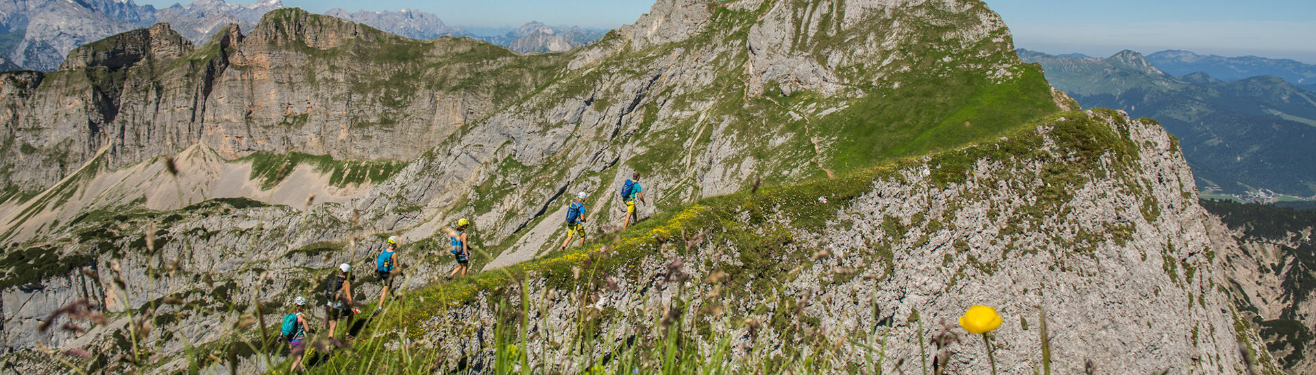 Klettersteiggehen im Rofangebirge am Achensee Eine Gruppe Klettersteigcampteilnehmer wandern in Richtung Hochiss bei strahlend blauem Himmel.