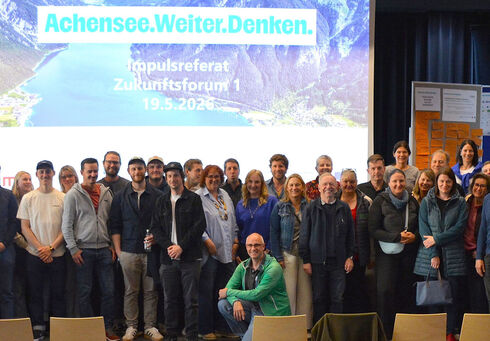 Gruppenfoto von den Teilnehmenden des Zukunftsforums „Achensee.Weiter.Denken.“ auf einer Bühne. Im Hintergrund ist eine große Leinwand mit der Aufschrift „Achensee.Weiter.Denken.“, „Impulsreferat Zukunftsforum 1“ und dem Datum „19.5.2026“ zu sehen.