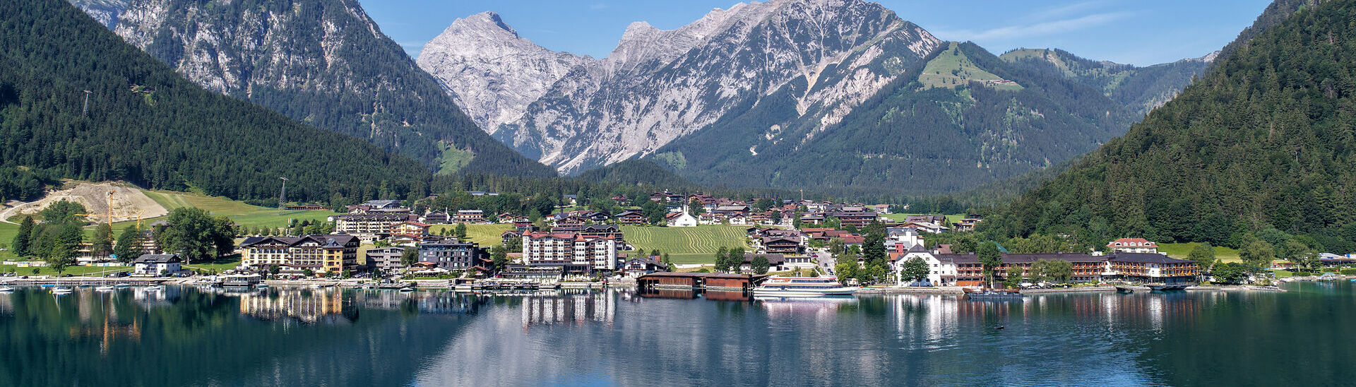 Blick über den Achensee auf Pertisau. Sanfte Wellen ziehen über das Wasser, während sich im Hintergrund die markanten Gipfel des Karwendelgebirges erheben und das Panorama prägen.