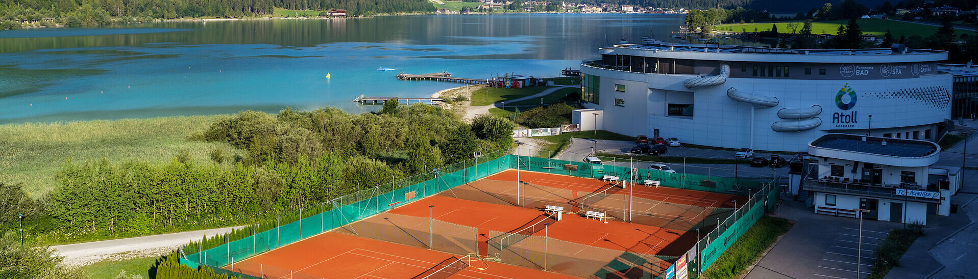 Blick auf die Tennisplätze in Maurach am Achensee vor türkisblauem Wasser des Achensees und der umliegenden Tiroler Bergwelt.