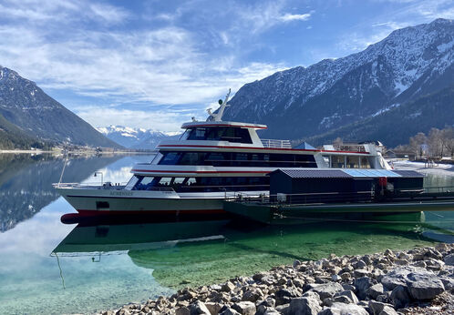 Die Achenseeschifffahrt legt hier in Pertisau am Achensee an. Im Hintergrund sind angezuckerte Berge wie das Ebner Joch zu sehen.