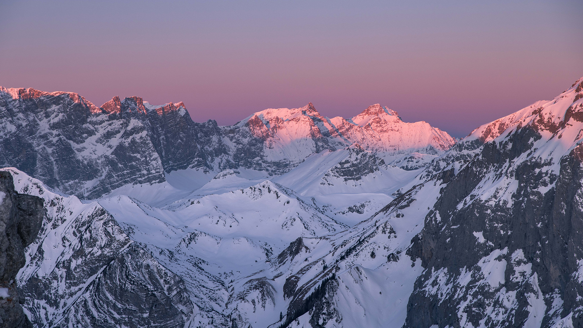 Der Blick auf den winterlichen Naturpark Karwendel bei Sonnenaufgang ist magisch. Die Gipfel und der Himmel färben sich violett und rosarot.